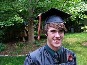 This picture shows a smiling young man wearing a graduation cap and gown.