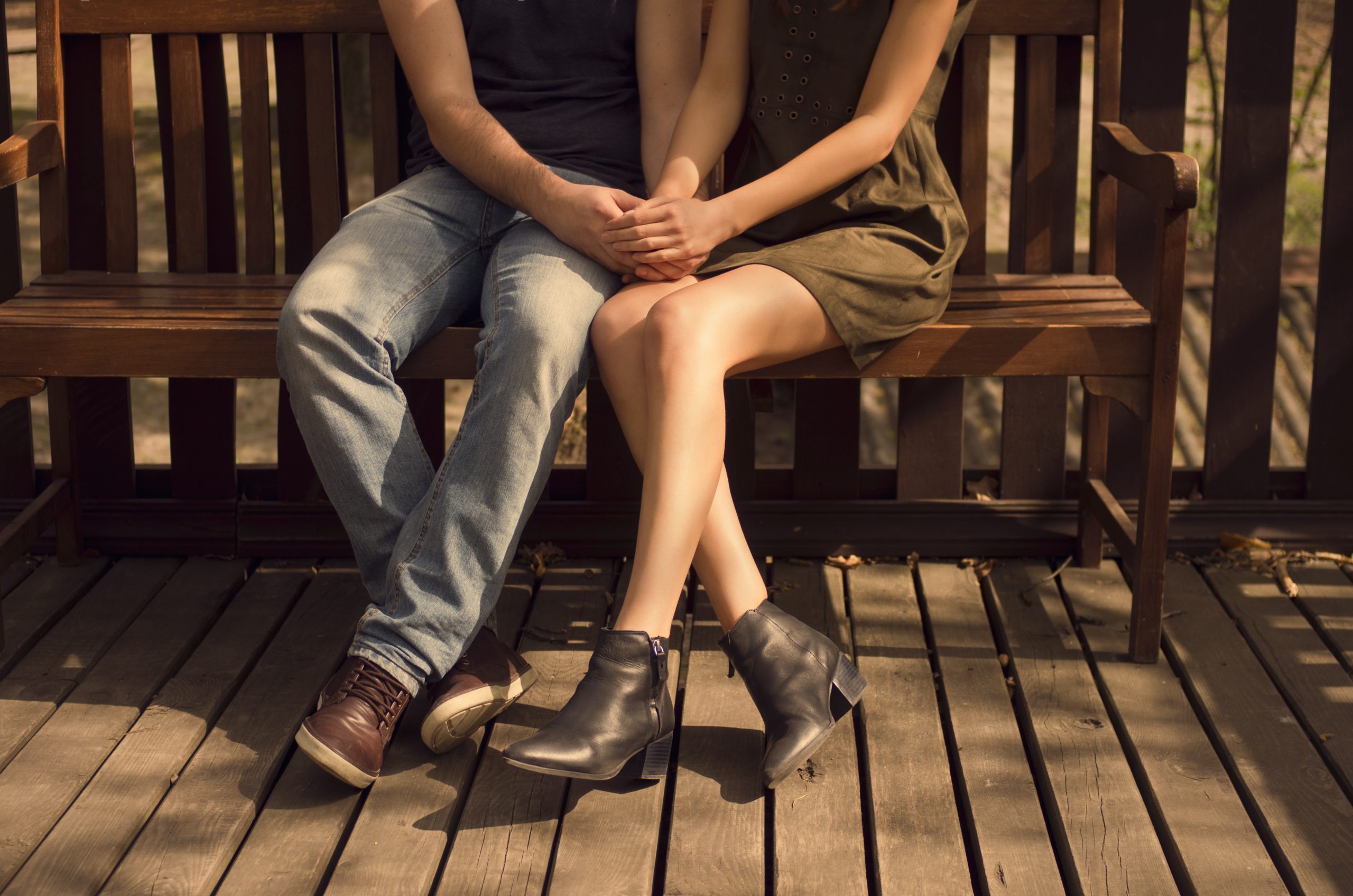 This picture shows a young couple holding hands while seated on a bench.