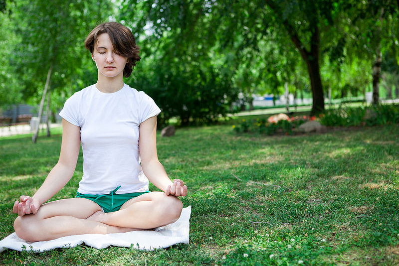 This picture shows a young woman meditating in a park.