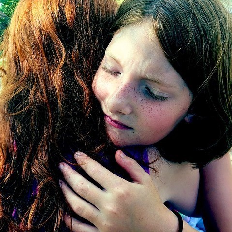 This picture shows a young girl with eyes closed hugging her friend.