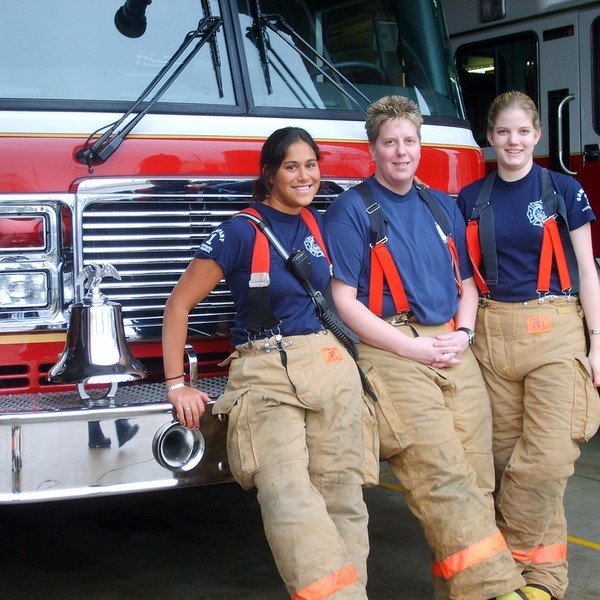 This picture shows three female members of a fire and rescue team stand in front of a fire engine wearing firefighting safety clothing.