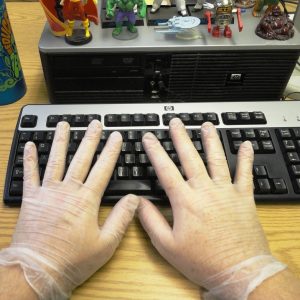 This picture shows a man's hands wearing latex gloves while typing on a computer keyboard.