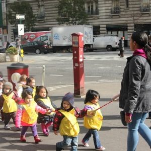 This picture shows a group of preschool students being led along a city street by an adult.