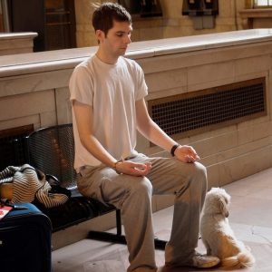 This picture shows a young man meditating on a bench in a train station.