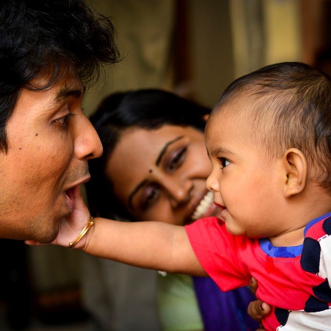 This picture shows a baby reaching out to touch the face of his smiling father as a happy mother looks on.